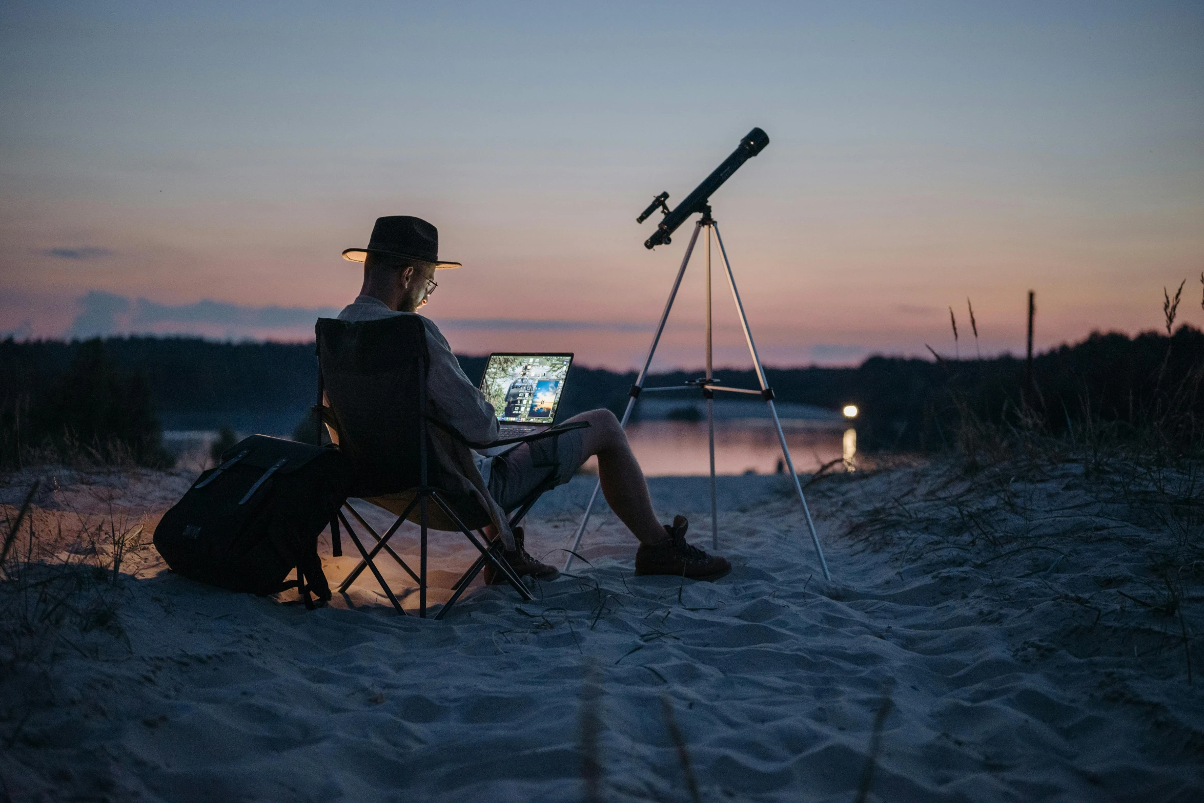 a man sitting on top of a beach next to a laptop computer, by Jan Tengnagel, unsplash contest winner, plein air, telescope, star charts, during an eclipse, on a canva