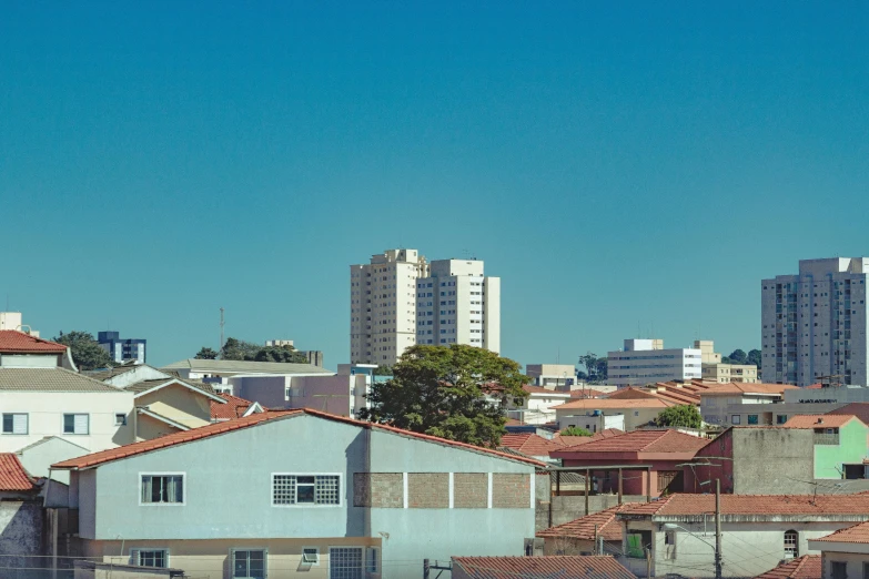 a train traveling through a city next to tall buildings, by Elsa Bleda, unsplash, hyperrealism, brazilian, clear blue sky vintage style, white houses, hiding in the rooftops