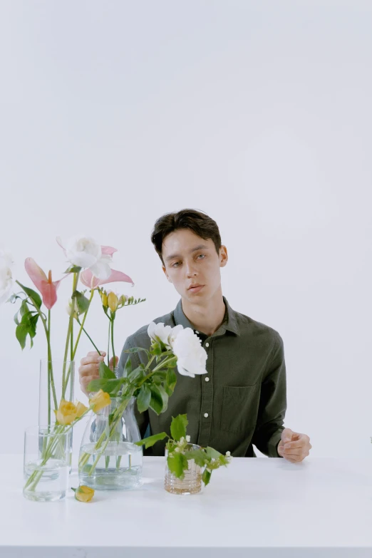 a man sitting at a table with flowers in vases, an album cover, inspired by Fei Danxu, young handsome pale roma, pose 4 of 1 6, video, ignant