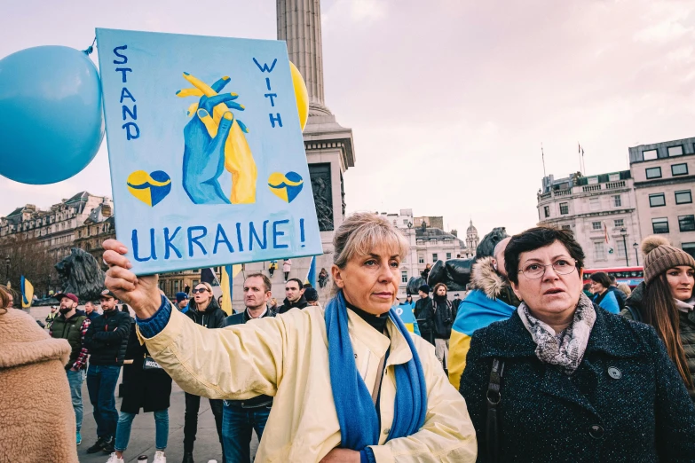 a woman holding a sign that says ukraine, by Julia Pishtar, square, uk, trending, group photo