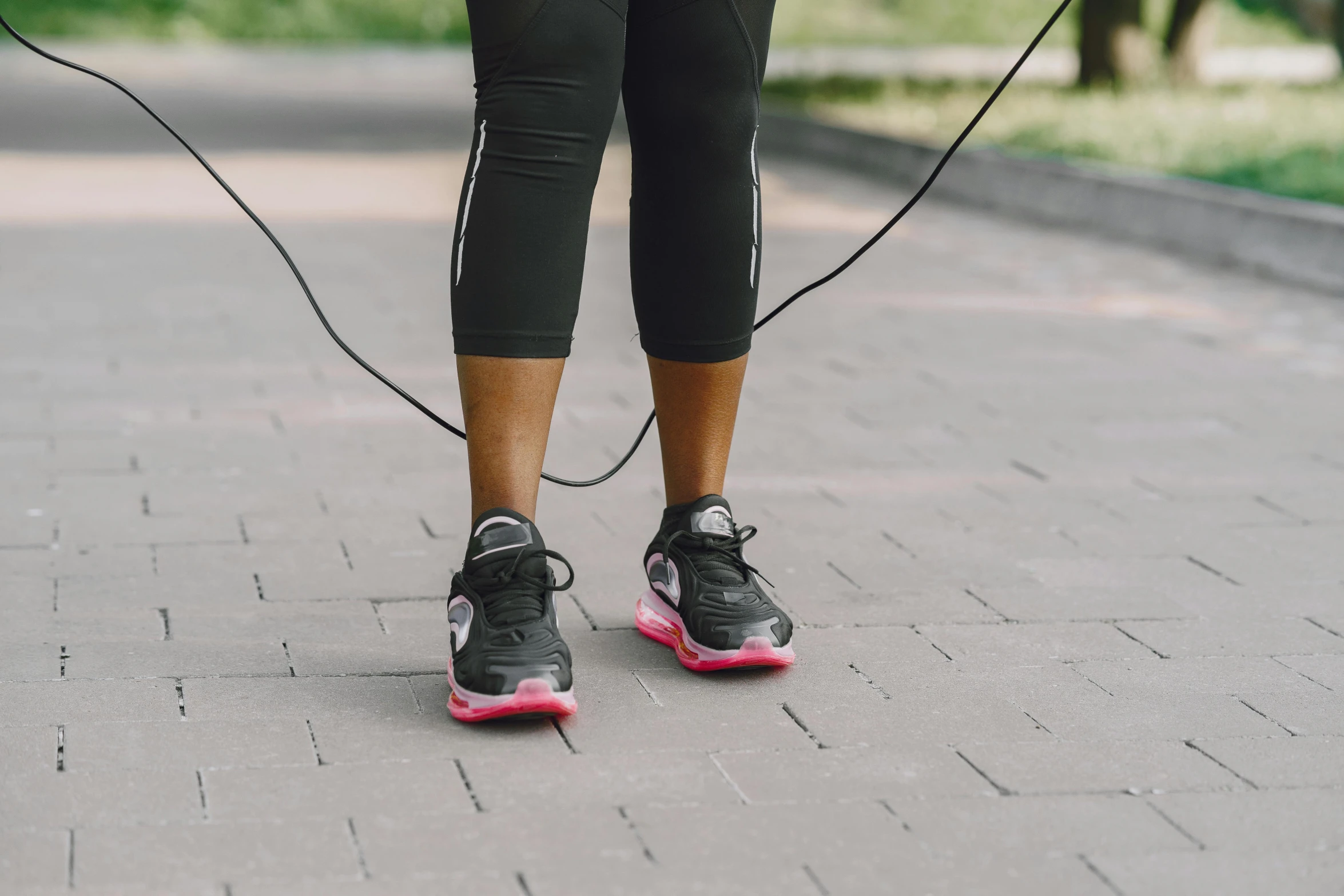 a woman standing on a sidewalk with a jump rope, pexels contest winner, neon pink and black color scheme, working out in the field, running shoes, black wired cables