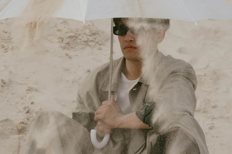 a man sitting in the sand holding an umbrella, off - white style, ryan jia, background image, shades