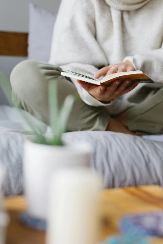 a woman sitting on a bed reading a book, trending on unsplash, on a coffee table, wearing a grey robe, wearing white pajamas, dynamic closeup