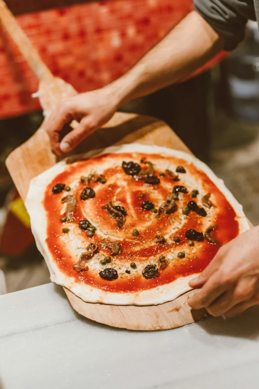 a person putting olives on a pizza on a wooden board, by Julia Pishtar, pexels contest winner, renaissance, an island made of red caviar, spiraling, woodfired, made of glazed