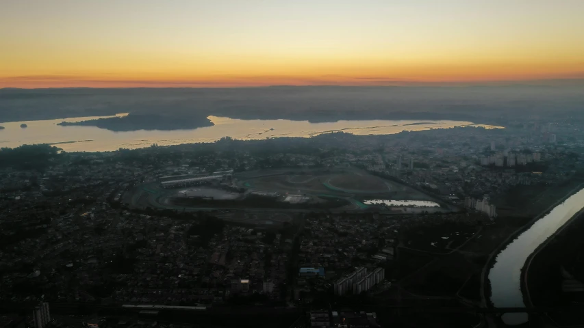 an aerial view of a city with a river running through it, by Attila Meszlenyi, pexels contest winner, hurufiyya, sun set, lake view, ground haze, split near the left