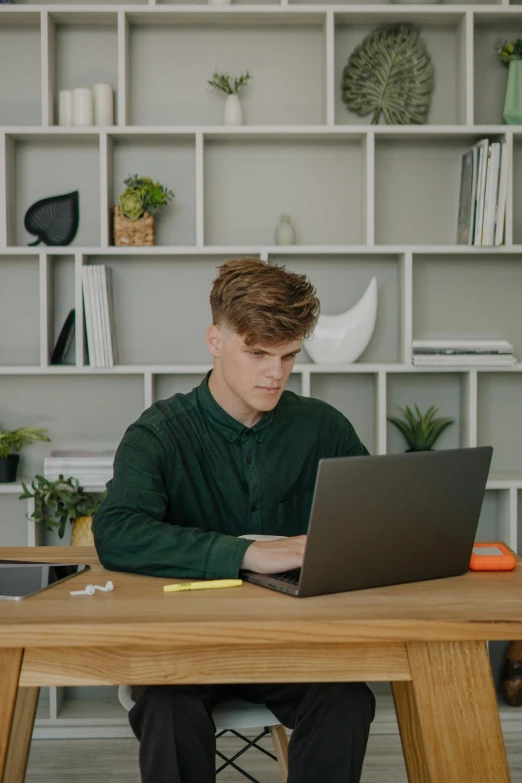 a man sitting at a table working on a laptop, slightly rounded face, liam, gen z, in an office