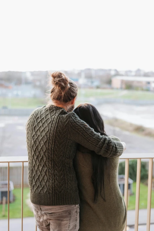 a couple of people standing on top of a balcony, trending on pexels, lesbian embrace, wearing a green sweater, from back, teenage girl