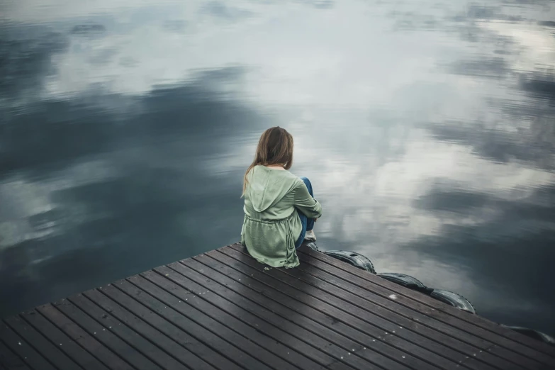 a woman sitting on a dock looking at the water, a picture, inspired by Elsa Bleda, pexels contest winner, romanticism, floating. greenish blue, looking sad, girl clouds, grey