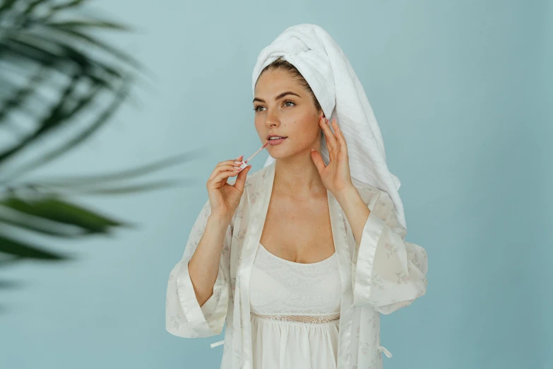 a woman with a towel on her head brushing her teeth, by Emma Andijewska, trending on pexels, in a silver silk robe, wearing long white robe, various posed, bedhead