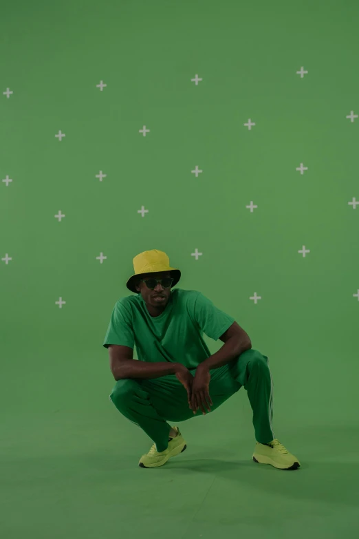 a man squatting in front of a green screen, inspired by Barkley Hendricks, pexels, video art, green hat, lil uzi vert, yellow and green, green floor