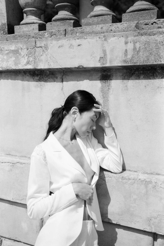 a black and white photo of a woman leaning against a wall, inspired by Marina Abramović, pexels contest winner, wearing white suit, sui ishida with black hair, paris, the girl and the sun