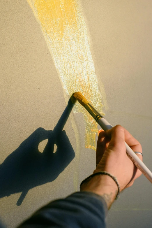 a person using a paint brush to paint a wall, a photorealistic painting, inspired by Lucio Fontana, trending on pexels, process art, golden hour sunlight, backlight, slight yellow hue, reflective surface