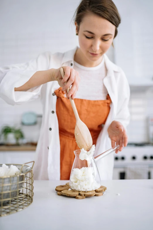 a woman in an orange apron is making marshmallows, inspired by Yukimasa Ida, trending on pexels, whipped cream, cone shaped, inside a glass jar, botanicals