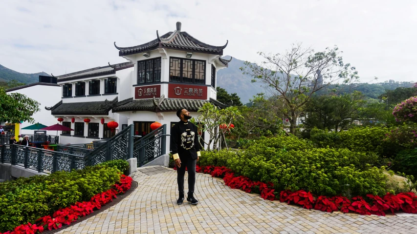 a man that is standing in front of a building, an album cover, inspired by Shen Quan, pexels contest winner, exterior botanical garden, chinese village, on a cloudy day, taiwan