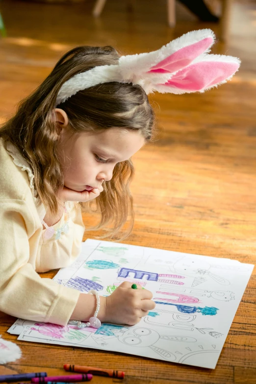 a little girl laying on the floor drawing with crayons, wearing a pink rabbit costume, colouring - in sheet, thumbnail, holding easter eggs