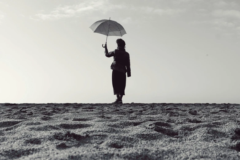 a person standing on a beach holding an umbrella, inspired by Max Dupain, unsplash, older woman, standing on a hill, masami suda, outside on the ground