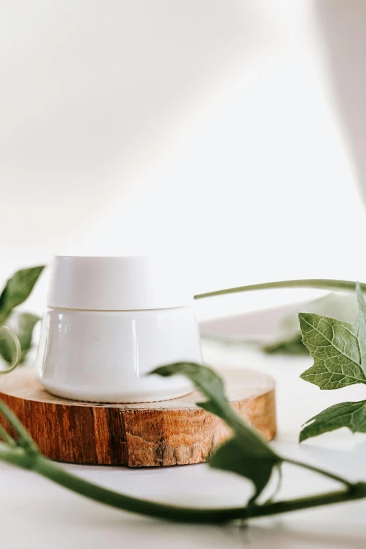 a white cup sitting on top of a wooden table, trending on pexels, lush greenery, detailed product image, jar on a shelf, light lighting side view