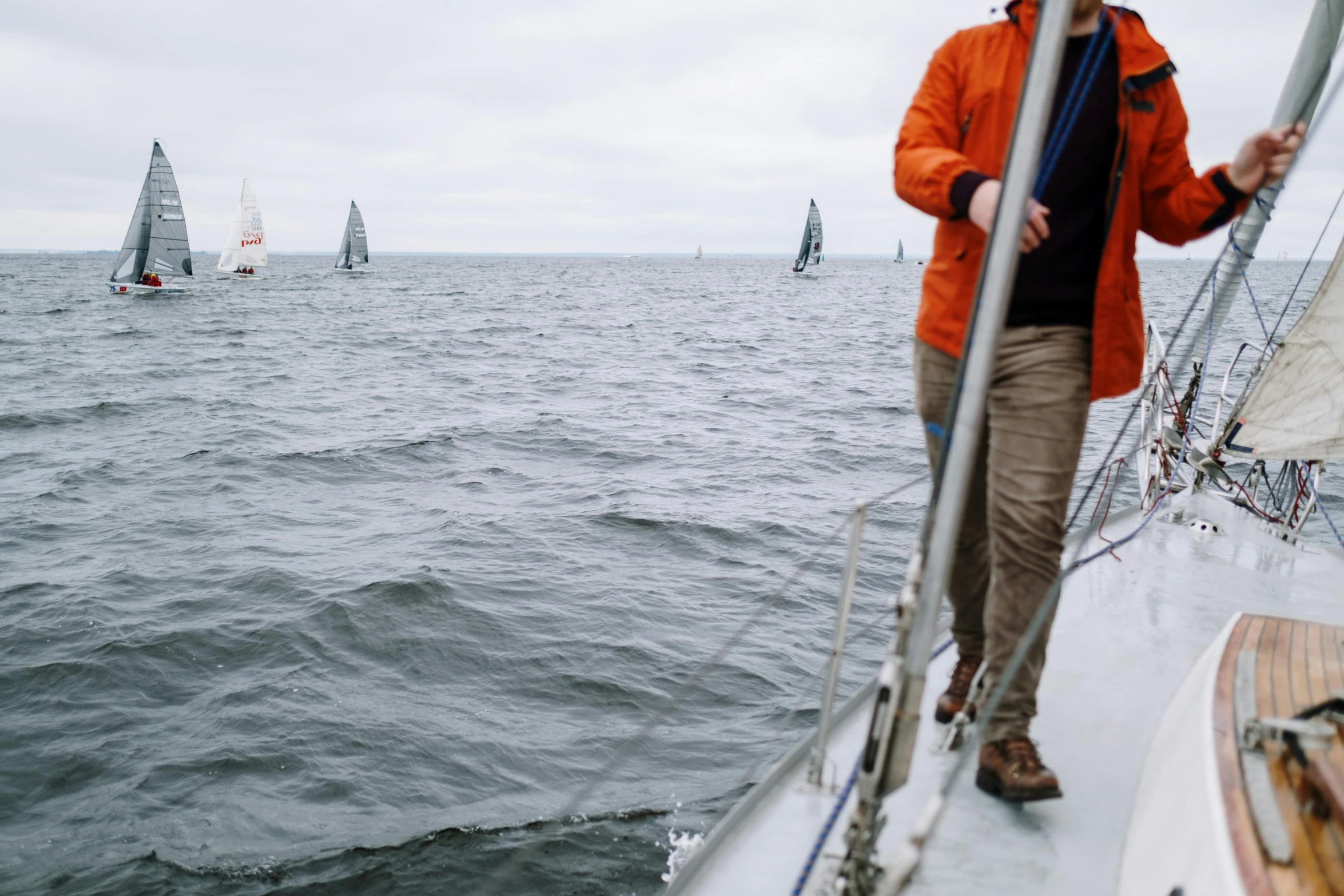 a man standing on the bow of a sailboat, pexels contest winner, happening, overcast, in a row, wearing jacket, tournament