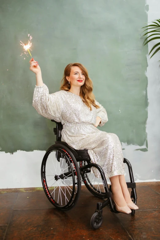 a woman in a wheelchair holding a sparkler, by Zofia Stryjenska, wearing a luxurious silk robe, liberty curls, wearing a baggy pajamas, glitter dress