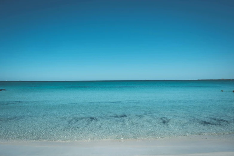 a large body of water sitting on top of a sandy beach, unsplash contest winner, minimalism, cloudless blue sky, the emerald coast, australian beach, fades to the horizon