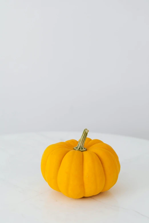 a small yellow pumpkin sitting on top of a white table, textured base ; product photos, hero prop, full-color, vanilla