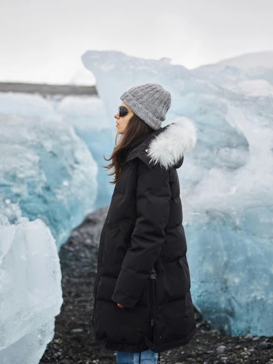 a woman standing in front of a group of icebergs, by Julia Pishtar, wearing hunter coat, close - up profile, black, made of ice