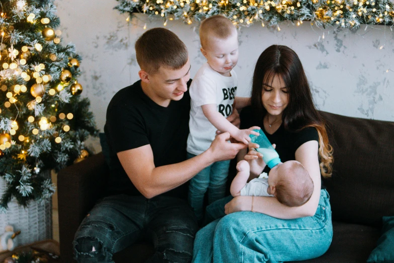 a man and woman sitting on a couch with a baby, by Adam Marczyński, pexels contest winner, russian, giving gifts to people, boys, a group of people