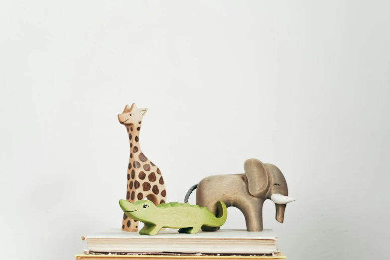 a toy giraffe sitting on top of a stack of books, inspired by Sarah Lucas, trending on unsplash, new sculpture, african elephants in the jungle, a wooden, three animals, product display photograph