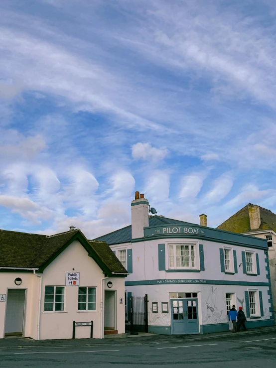 a large white building sitting on the side of a road, by Rachel Reckitt, pexels contest winner, panorama view of the sky, old shops, swirley clouds, picton blue