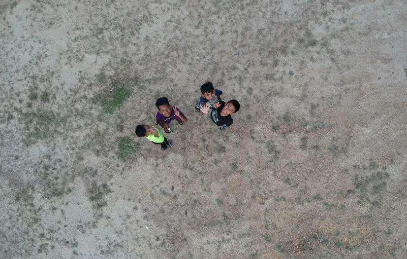 a group of children sitting on top of a dirt field, bad drone camera, shot from 5 0 feet distance, floating in the air, thawan duchanee