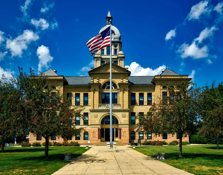 a large building with a flag on top of it, a colorized photo, by Andrew Domachowski, shutterstock, beautiful small town, official courthouse, prairie, stunning grand architecture