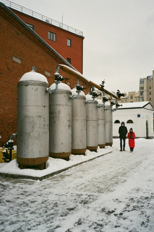 a couple of people walking down a snow covered street, inspired by Stanislav Zhukovsky, temporary art, propane tanks, opposite the lift-shaft, white wall complex, 1996)