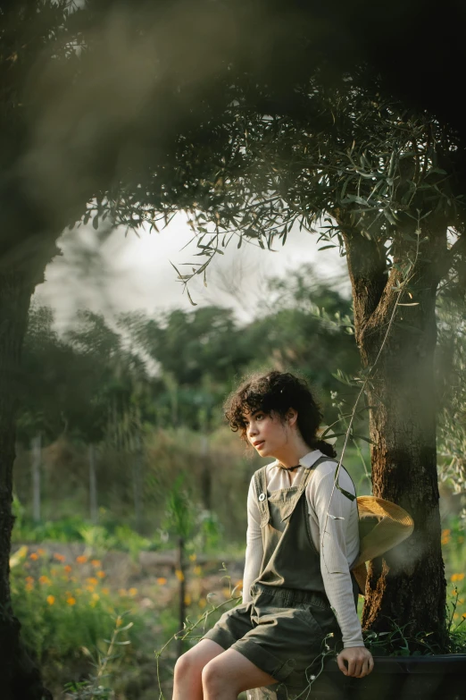 a woman sitting on a bench next to a tree, finn wolfhard, lots of oak and olive trees, soft light, farming