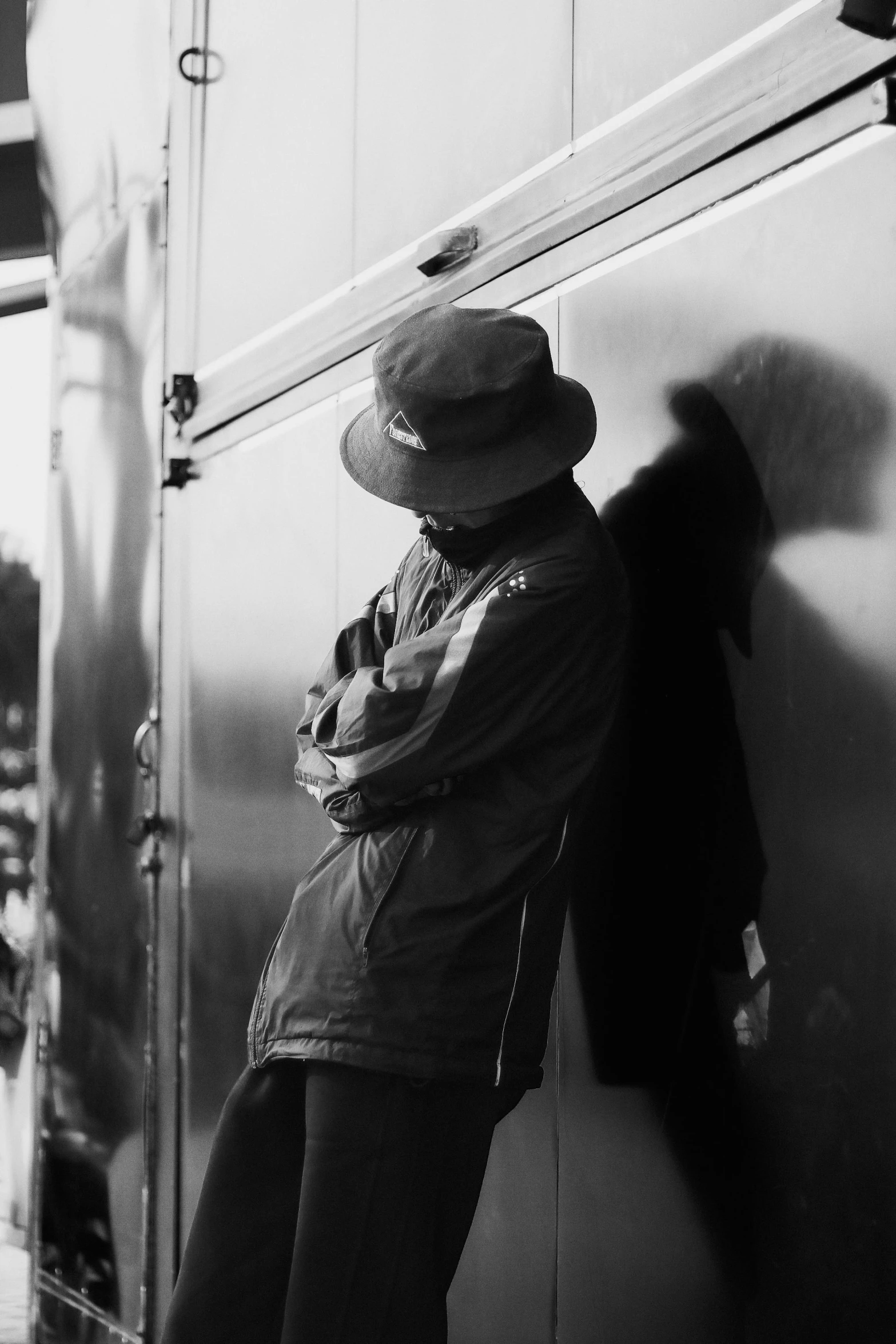 a black and white photo of a man leaning against a wall, inspired by Louis Faurer, unsplash, hat and hoodie, sundown, eyes closed, reflection