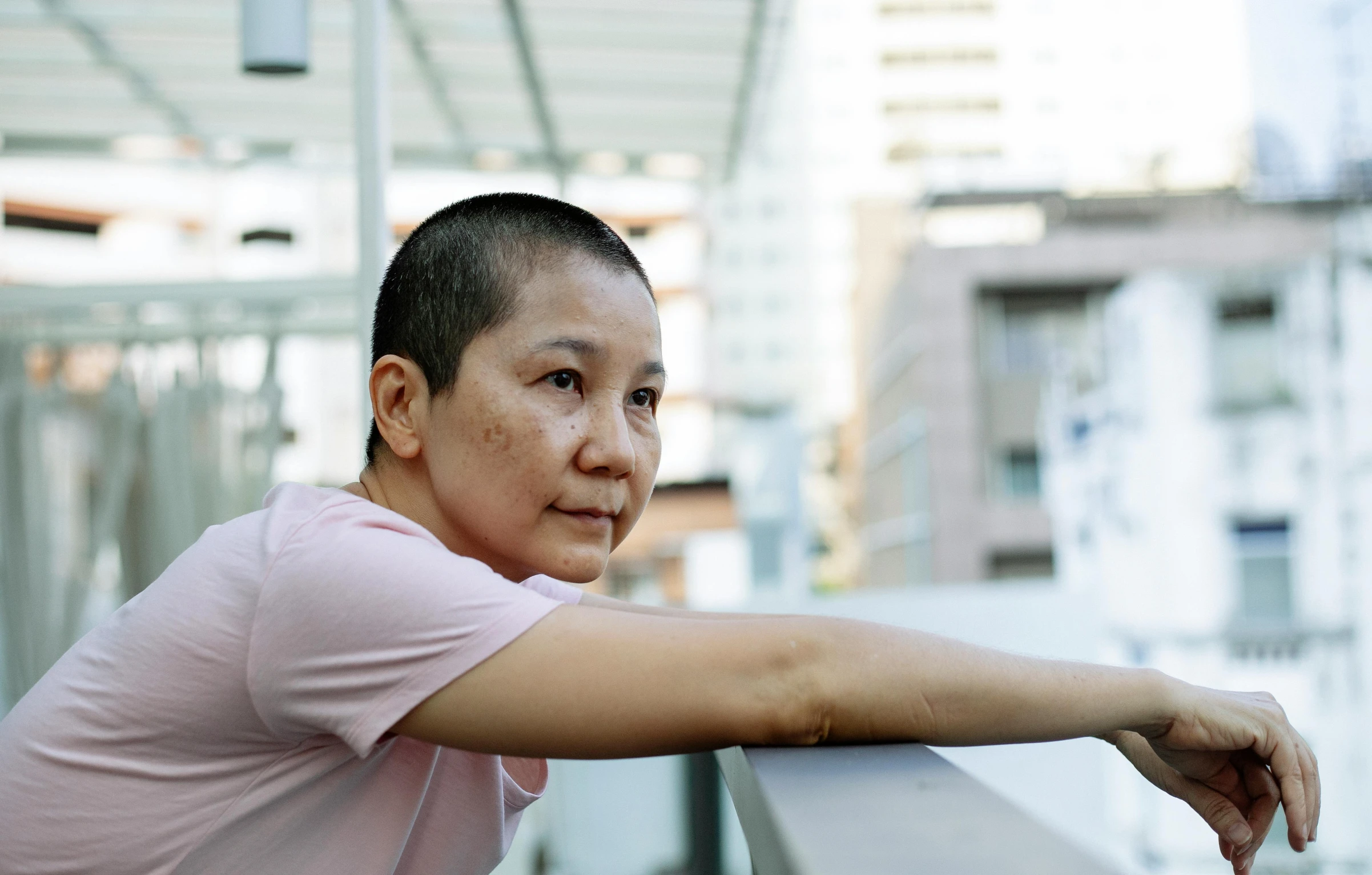 a woman in a pink shirt leaning on a railing, a portrait, inspired by Ruth Jên, pexels contest winner, happening, shaved face, cai guo-qiang, aged 4 0, looking from shoulder