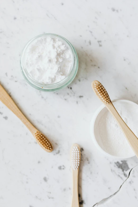 a couple of toothbrushes sitting next to a jar of toothpaste, trending on unsplash, renaissance, natural materials, covered in white flour, on a white table, jen atkin