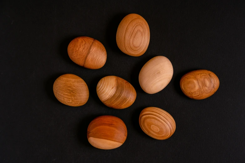 a group of wooden eggs sitting on top of a black surface, an album cover, inspired by Agnes Martin, unsplash, cedar, cherry, group of seven, organic shapes