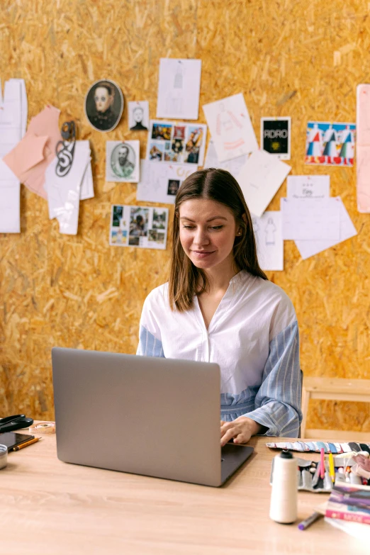 a woman sitting at a table working on a laptop, trending on pexels, arbeitsrat für kunst, standing on a desk, post graduate, slightly smiling, cardboard