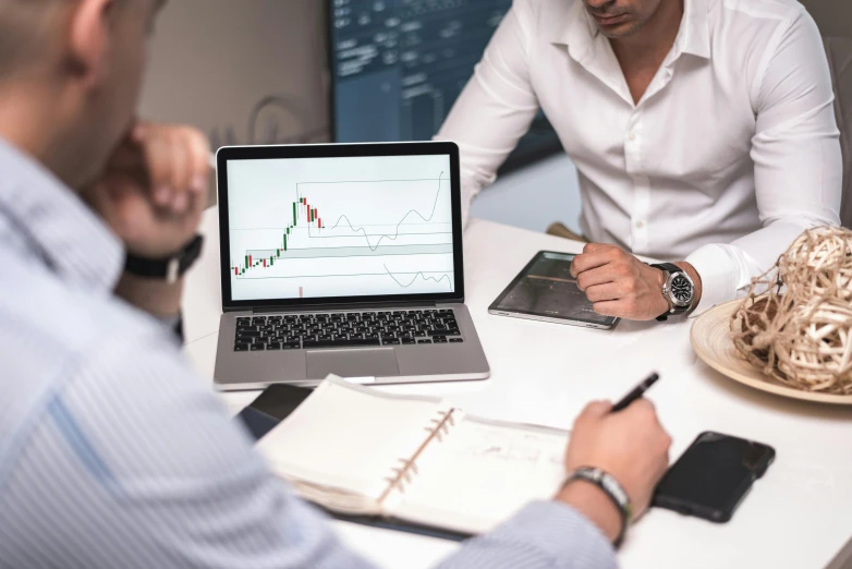 two men sitting at a table looking at a laptop, pexels contest winner, analytical art, displaying stock charts, no - text no - logo, qirex, wide screenshot