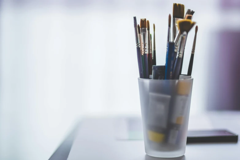 a cup filled with brushes sitting on top of a table, pexels contest winner, academic art, fan favorite, paint tubes, pristine and clean design, white wall coloured workshop