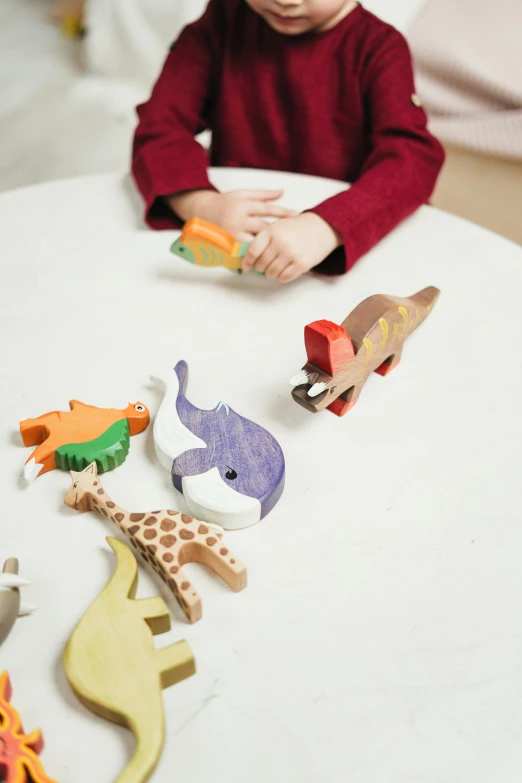 a little boy sitting at a table playing with wooden animals, a jigsaw puzzle, by Paul Bird, trending on pexels, detailed product image, detail shot, whales, over his shoulder