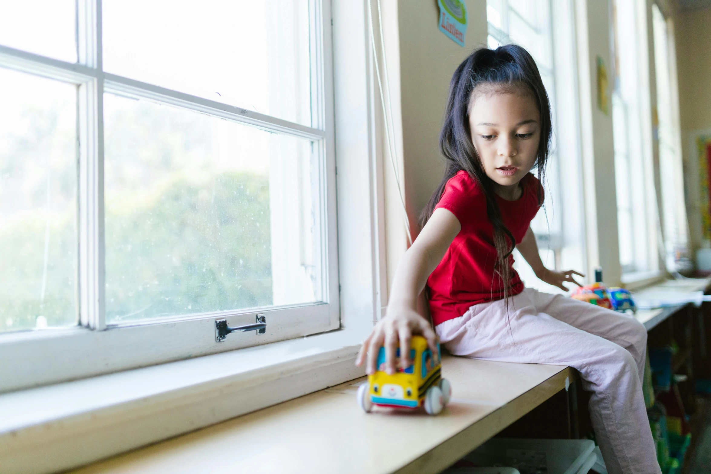 a little girl sitting on a window sill playing with a toy truck, pexels contest winner, square, a young asian woman, sitting at table, schools