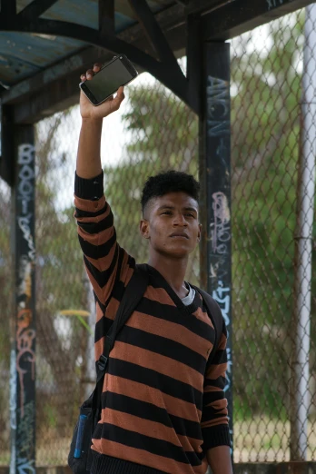 a man standing on top of a tennis court holding a racquet, an album cover, inspired by Byron Galvez, unsplash, graffiti, wearing stripe shirt, hold up smartphone, black teenage boy, headshot photo