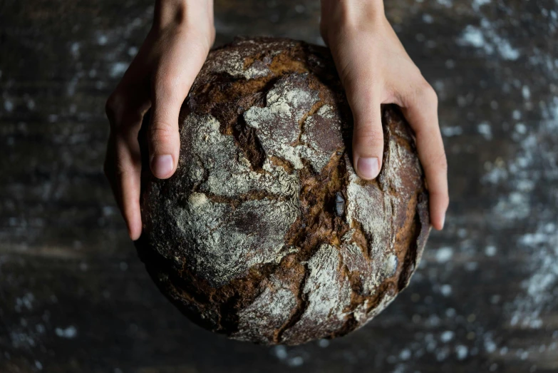 a person holding a loaf of bread in their hands, by Helen Stevenson, unsplash, process art, round format, “ iron bark, dark and intricate, holding a ball