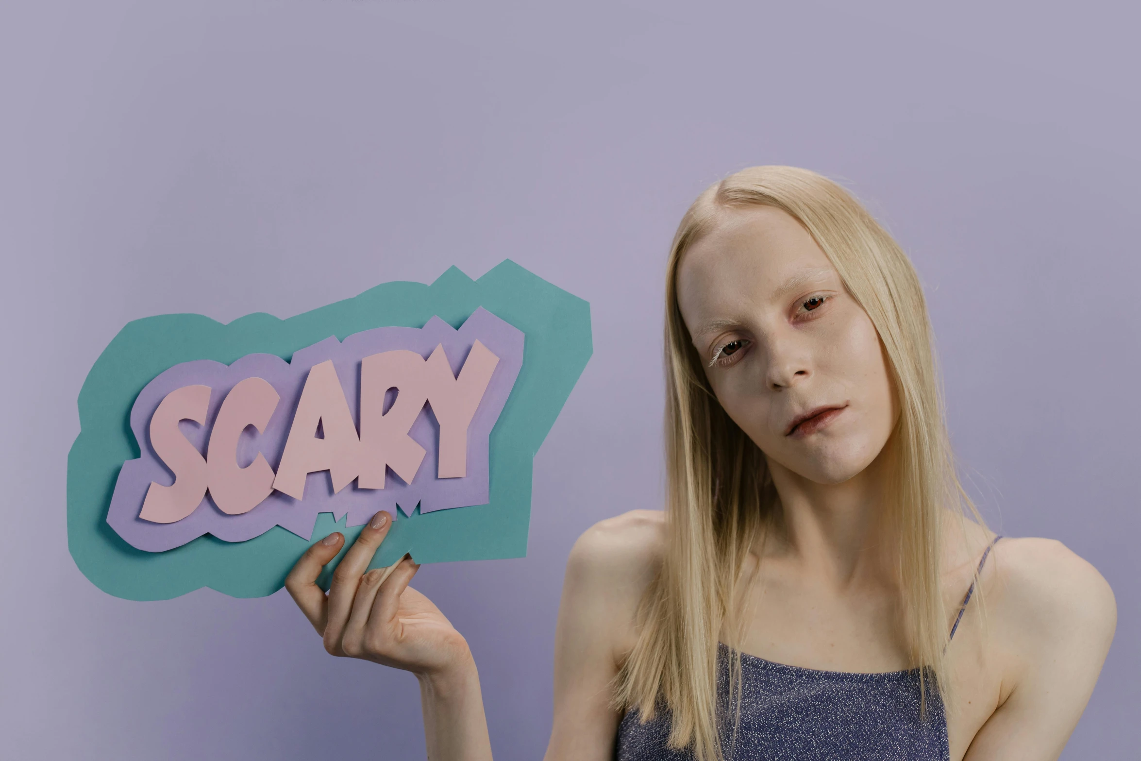 a woman holding a sign that says scary, an album cover, inspired by Ignacy Witkiewicz, pop surrealism, with a white complexion, pastel', in claymation, photo from a promo shoot