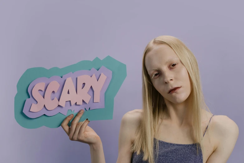 a woman holding a sign that says scary, an album cover, inspired by Ignacy Witkiewicz, pop surrealism, with a white complexion, pastel', in claymation, photo from a promo shoot