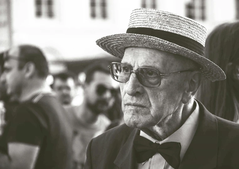 a black and white photo of a man wearing a hat, inspired by Josef Navrátil, pexels contest winner, bauhaus, wearing straw hat, crowd, old man, jewish young man with glasses