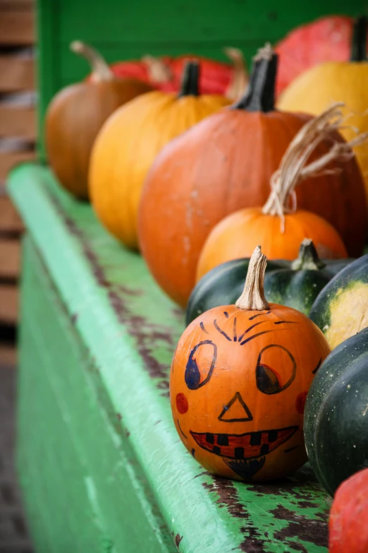 a row of pumpkins with faces painted on them, by Everett Warner, pexels, square, a green, color picture, cornucopia