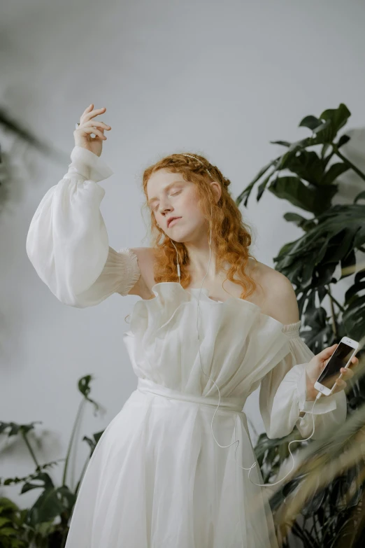 a woman in a white dress standing next to a plant, an album cover, inspired by Alexandre Cabanel, trending on pexels, renaissance, ginger wavy hair, goddess checking her phone, waving robe movement, albino white pale skin