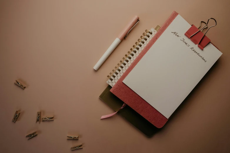 a notepad sitting on top of a desk next to a pencil, by Emma Andijewska, trending on pexels, brown and pink color scheme, book cover, red and white color theme, thumbnail